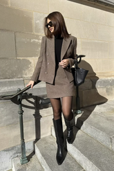 a lady in a black knit top, and a brown blazer and skirt suit